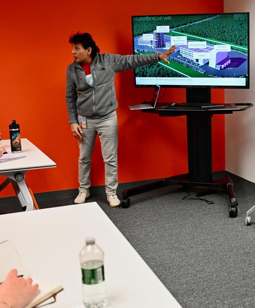 Yogesh Sharma pointing to a manufacturing facility rendering on a screen during class